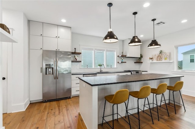 kitchen with a wealth of natural light, stainless steel refrigerator with ice dispenser, light hardwood / wood-style floors, and white cabinets