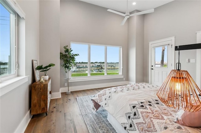 bedroom with recessed lighting, wood-type flooring, a high ceiling, and baseboards