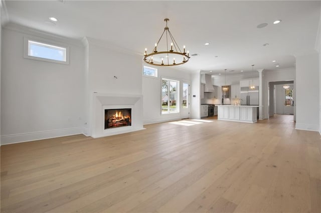 unfurnished living room with an inviting chandelier, ornamental molding, and light hardwood / wood-style floors