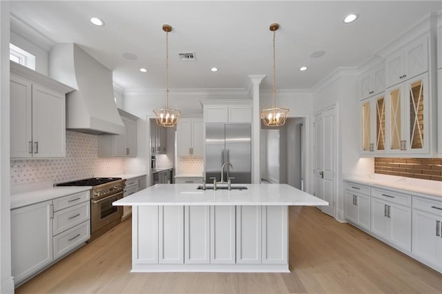 kitchen featuring a chandelier, high end appliances, premium range hood, and a sink
