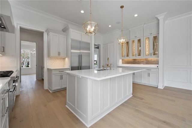 kitchen featuring a kitchen island with sink, light hardwood / wood-style flooring, stainless steel appliances, sink, and decorative light fixtures