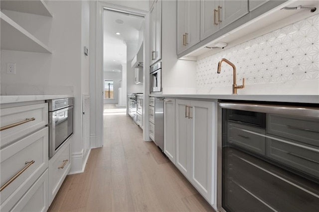 kitchen featuring tasteful backsplash, stainless steel oven, white cabinetry, light hardwood / wood-style flooring, and sink