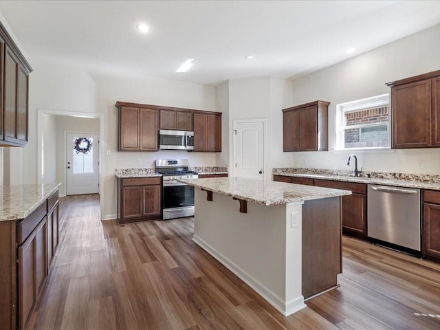 kitchen featuring a kitchen island, dark hardwood / wood-style flooring, stainless steel appliances, and light stone counters