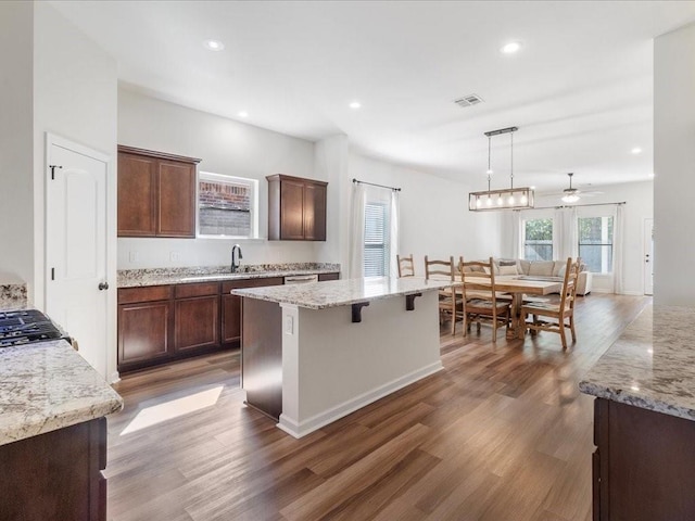 kitchen with light stone countertops, decorative light fixtures, dark hardwood / wood-style floors, and a kitchen island