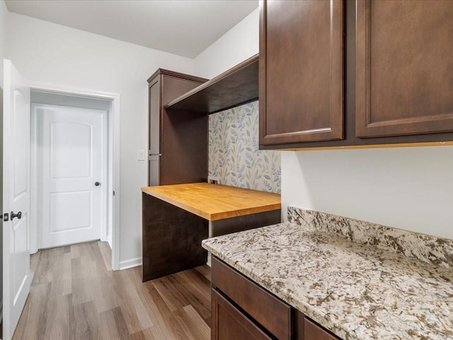 kitchen with dark brown cabinetry, light stone countertops, and light hardwood / wood-style floors