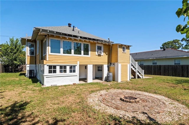 rear view of property featuring a lawn, cooling unit, and a fire pit