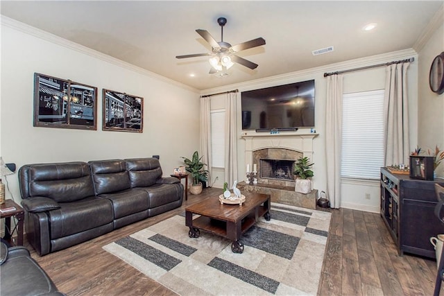 living room featuring ceiling fan, a tile fireplace, dark hardwood / wood-style floors, and crown molding