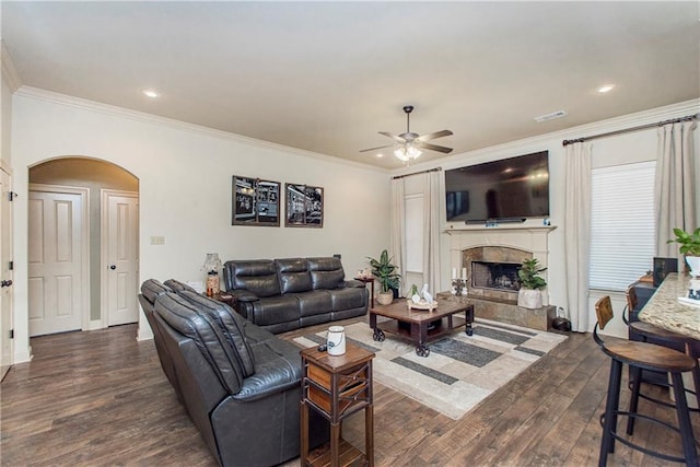 living room with crown molding, a tiled fireplace, dark hardwood / wood-style floors, and ceiling fan