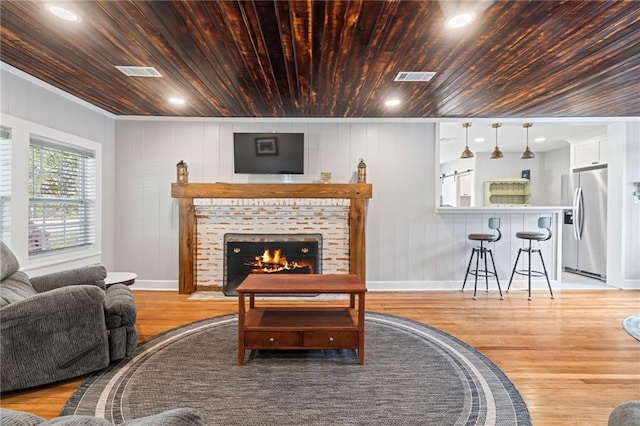 living room with crown molding, light wood-type flooring, a fireplace, and wooden ceiling