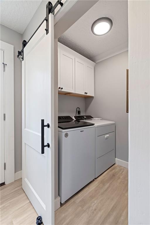 washroom featuring a barn door, cabinets, washer and dryer, and light hardwood / wood-style floors