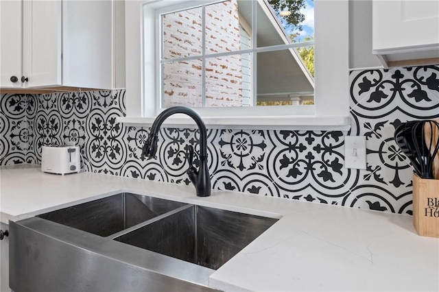 interior details featuring decorative backsplash, sink, and white cabinets