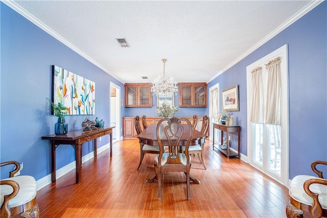 dining area featuring a textured ceiling, ornamental molding, hardwood / wood-style floors, and a chandelier