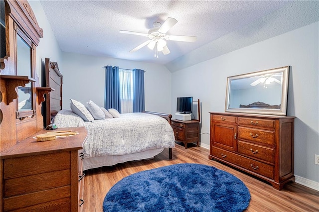 bedroom featuring light hardwood / wood-style flooring, vaulted ceiling, ceiling fan, and a textured ceiling