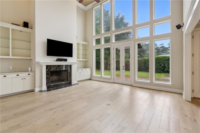 unfurnished living room with a premium fireplace, built in features, a towering ceiling, light hardwood / wood-style floors, and ceiling fan