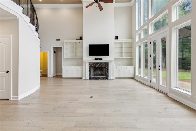 unfurnished living room featuring light wood-type flooring, a fireplace, ceiling fan, a high ceiling, and crown molding