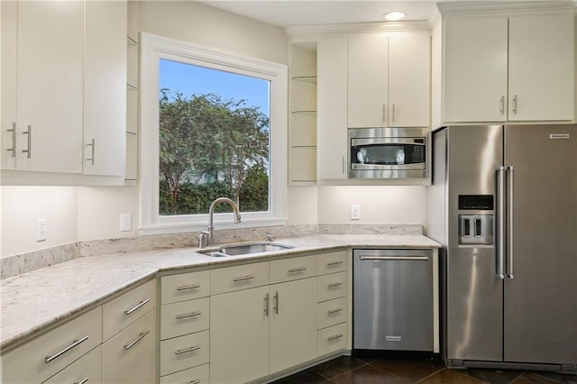 kitchen featuring stainless steel appliances, light stone countertops, sink, and dark tile patterned floors