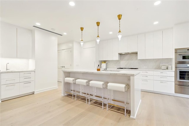 kitchen featuring a center island with sink, light hardwood / wood-style floors, white cabinetry, and pendant lighting