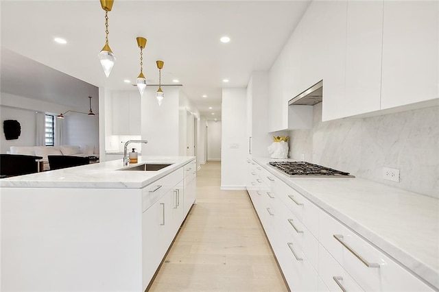 kitchen featuring an island with sink, hanging light fixtures, sink, white cabinetry, and stainless steel gas stovetop