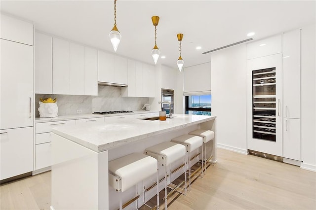 kitchen with an island with sink, light wood-type flooring, white cabinetry, and decorative light fixtures