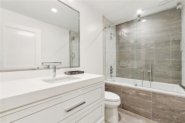 full bathroom with enclosed tub / shower combo, vanity, and toilet