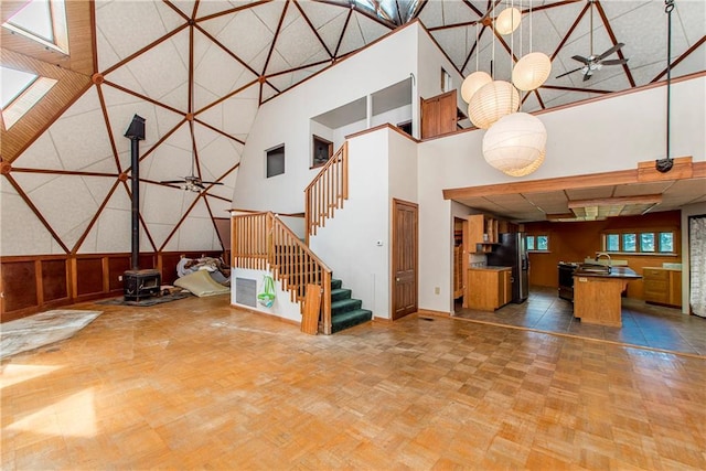 unfurnished living room featuring ceiling fan, a skylight, a high ceiling, and a wood stove