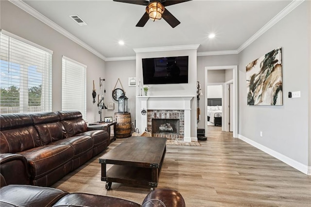 living room with ornamental molding, light wood-type flooring, ceiling fan, and a fireplace