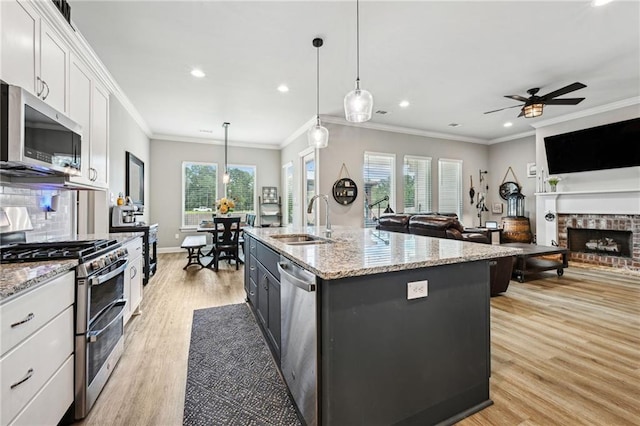 kitchen with stainless steel appliances, white cabinetry, decorative light fixtures, a kitchen island with sink, and light wood-type flooring