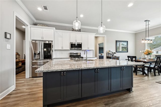 kitchen featuring white cabinetry, decorative light fixtures, a center island with sink, and stainless steel appliances