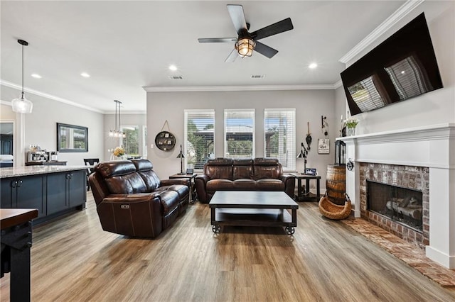 living room featuring ornamental molding, light wood-type flooring, a fireplace, and ceiling fan with notable chandelier