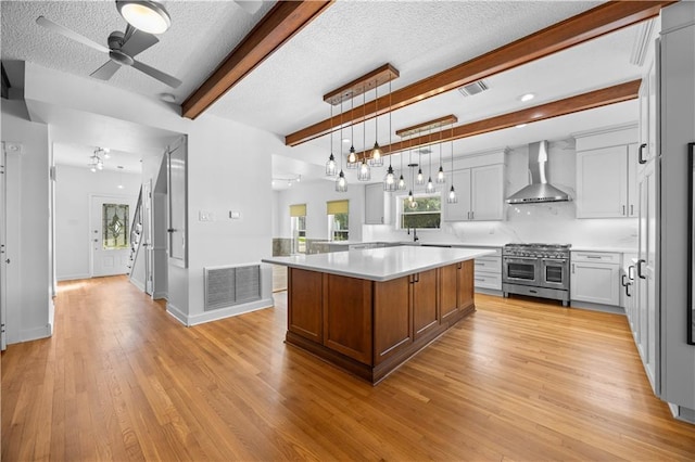 kitchen with beam ceiling, a kitchen island, wall chimney exhaust hood, double oven range, and light wood-type flooring