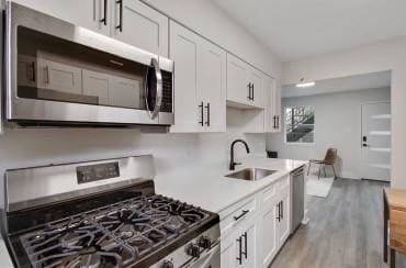 kitchen featuring appliances with stainless steel finishes, white cabinetry, sink, and light hardwood / wood-style flooring