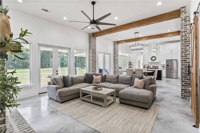 living room featuring french doors, beamed ceiling, ceiling fan with notable chandelier, and a barn door