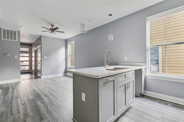 kitchen featuring ceiling fan, a kitchen island with sink, sink, decorative light fixtures, and light hardwood / wood-style floors