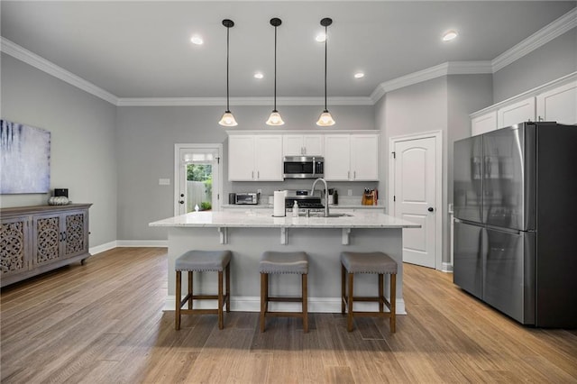 kitchen featuring light hardwood / wood-style floors, white cabinetry, an island with sink, pendant lighting, and stainless steel appliances