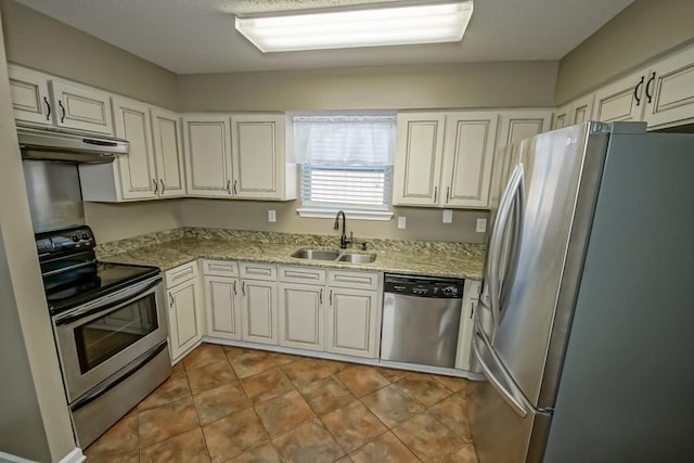 kitchen with stainless steel appliances, white cabinetry, light stone counters, and sink