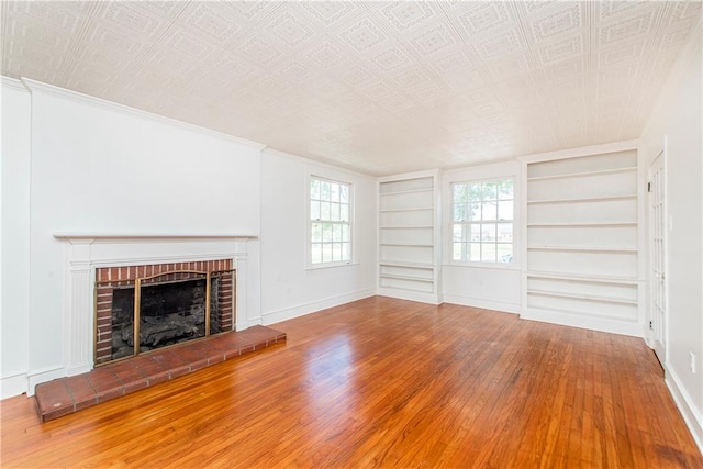 unfurnished living room featuring wood-type flooring, ornamental molding, built in features, and a brick fireplace