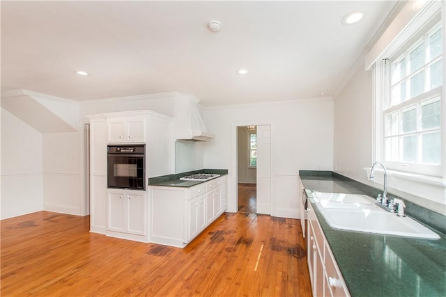 kitchen with light hardwood / wood-style floors, sink, white cabinetry, oven, and premium range hood