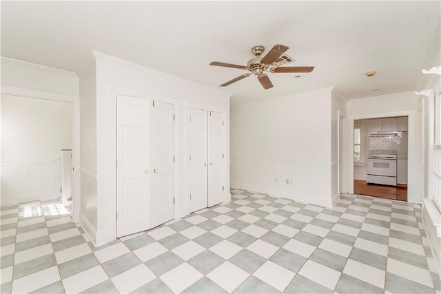 unfurnished bedroom with ornamental molding, ceiling fan, and multiple closets