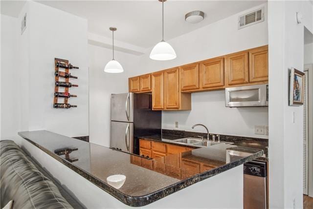 kitchen with stainless steel appliances, dark stone counters, kitchen peninsula, sink, and pendant lighting