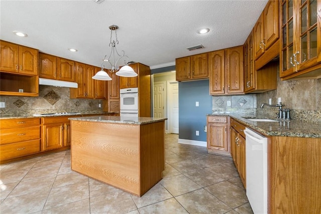 kitchen featuring stone counters, a center island, tasteful backsplash, pendant lighting, and white appliances