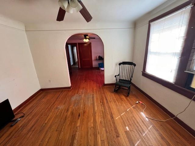 unfurnished room featuring baseboards, wood finished floors, arched walkways, and ceiling fan