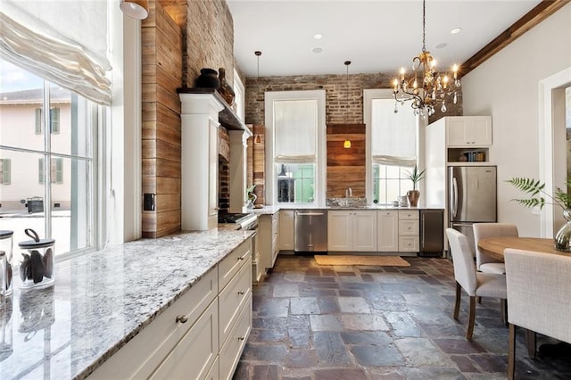 kitchen featuring ornamental molding, white cabinetry, appliances with stainless steel finishes, decorative light fixtures, and light stone countertops