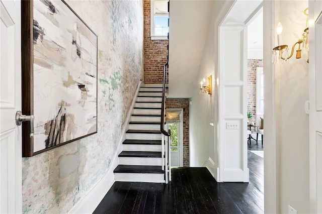 staircase featuring brick wall, a high ceiling, and hardwood / wood-style flooring