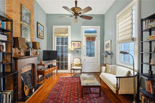 sitting room featuring a brick fireplace, wood-type flooring, and ceiling fan