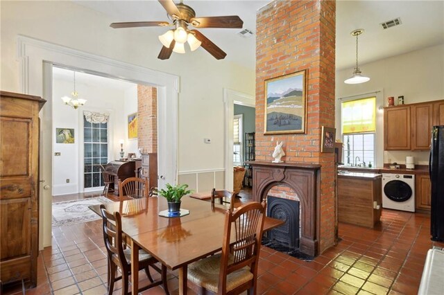 dining area featuring dark tile patterned flooring, sink, washer / dryer, a large fireplace, and ceiling fan with notable chandelier