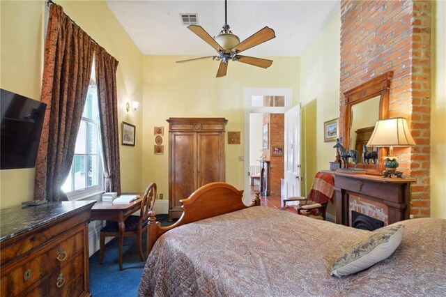 bedroom featuring a fireplace, dark carpet, and ceiling fan