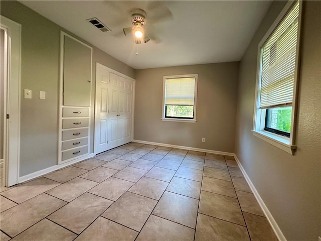 unfurnished bedroom with light tile patterned flooring, a closet, ceiling fan, and multiple windows