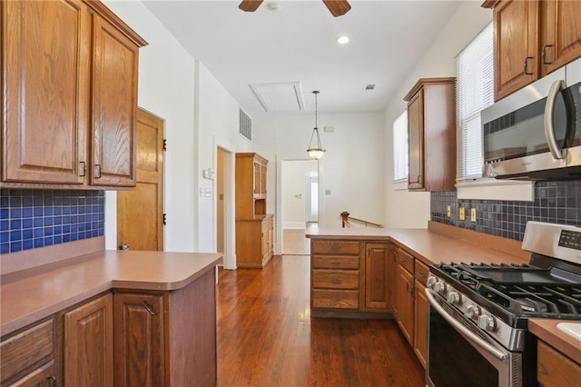 kitchen featuring pendant lighting, kitchen peninsula, stainless steel appliances, backsplash, and dark hardwood / wood-style flooring