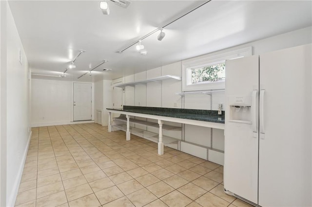 basement with rail lighting, white fridge with ice dispenser, and light tile patterned floors