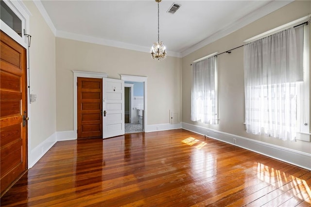 empty room featuring ornamental molding, an inviting chandelier, and dark wood-type flooring